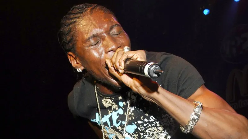 Getty Images A black man with short cornrows holds a microphone to his lips as he performs on stage. His eyes are closed, suggesting a passionate performance. He wears a large ring on one finger, has two hoop earrings in one ear, and wears a long silver chain over a black t-shirt with an elaborate, colourful design. The arm holding the mic has a large, chunky silver bangle around the wrist.
